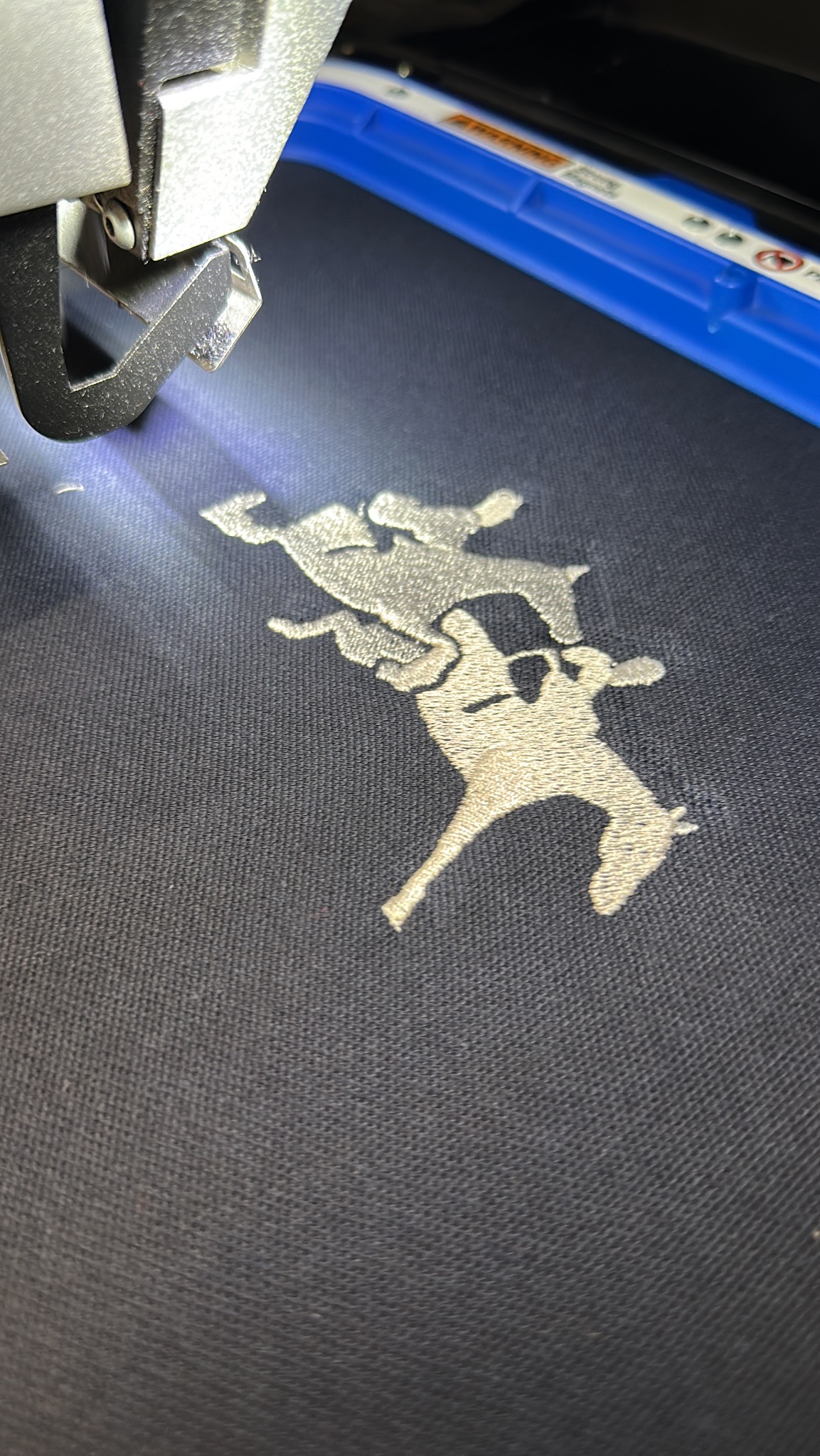 Proces tworzenia haftu maszynowego: igła maszyny precyzyjnie nanosi wzór dwóch koni na ciemny materiał.