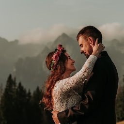 Dreamcatchers Kuba&Ula Jakub Ćwiklewski Fotograf Ełk - Para młoda w objęciach na tle górskim, panna młoda z wiankiem z różowych kwiatów i suknią z koronkowymi rękawami, pan młody w ciemnym garniturze, ciepłe światło zachodzącego słońca.