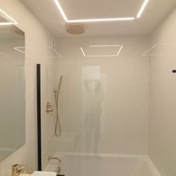 Paweł Wegner - Nowoczesna łazienka z wanną obudowaną czarnym marmurem, złotą armaturą i podświetlanym sufitem LED w kształcie prostokąta.