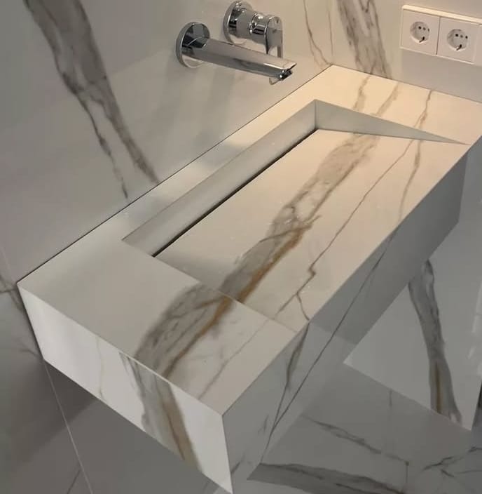 Nowoczesna umywalka z białego marmuru z wyraźnymi żyłami, wbudowana w blat z tego samego materiału, chromowana bateria ścienna i dopasowane płytki marmurowe na ścianie i podłodze, minimalistyczny...
