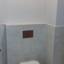 Олександр Даховський - Nowoczesna, podwieszana toaleta z brązowym panelem spłukującym na tle szarych, matowych płytek w wykończonej łazience. Minimalistyczny design.