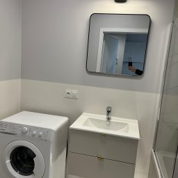 Олександр Даховський - Nowoczesna łazienka z pralką, umywalką z szafką w odcieniach szarości i lustrem. Minimalistyczne oświetlenie i płytki w dwóch odcieniach szarości.