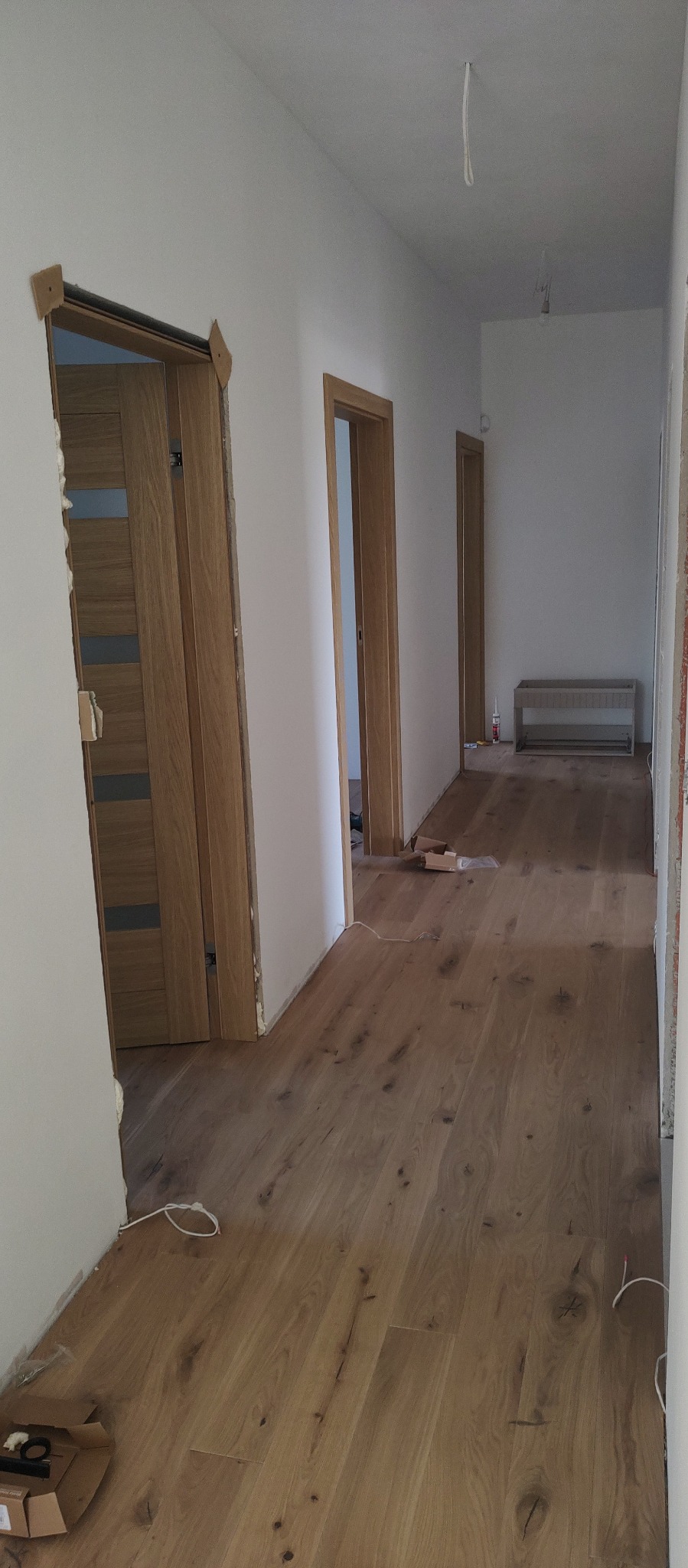 Korytarz z drewnianą podłogą i zamontowanymi drzwiami z drewnianymi ościeżnicami. Widoczne ślady po pracach wykończeniowych.