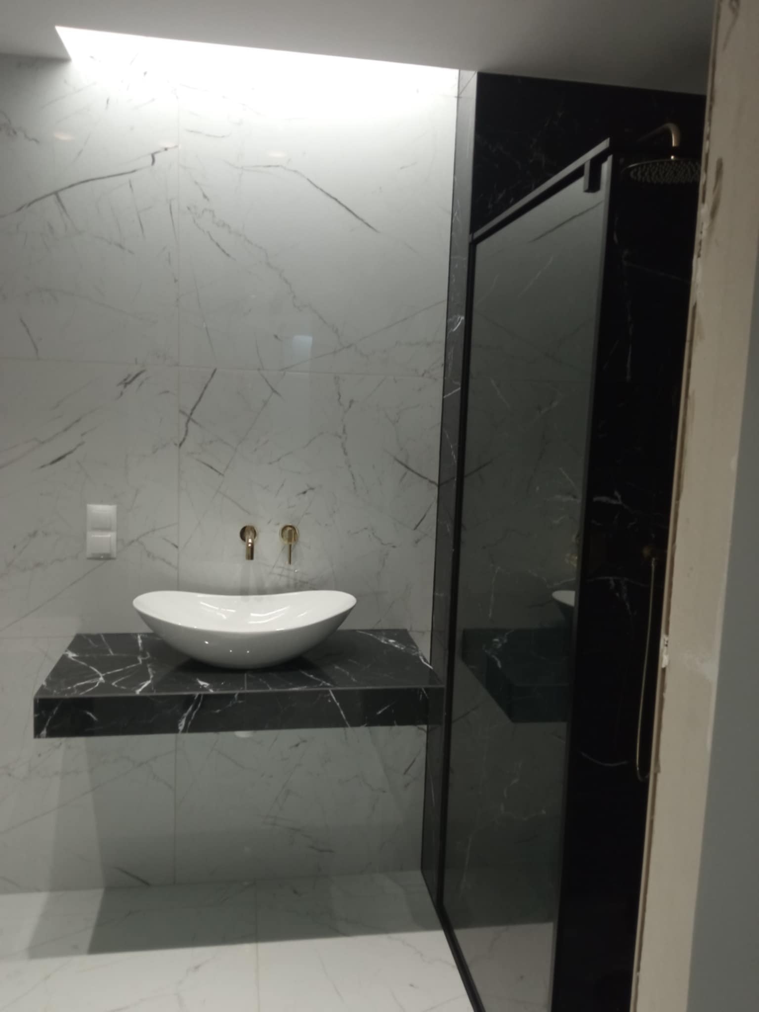 Elegancka łazienka z umywalką nablatową na czarnym blacie marmurowym, białe płytki imitujące marmur na ścianach i kabina prysznicowa.