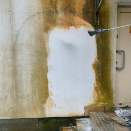 VORTEXO JAROSŁAW BEDNAREK - Mycie elewacji budynku z wyraźnymi zabrudzeniami, czyszczenie za pomocą myjki ciśnieniowej, widoczne efekty pracy, schody i fragment drzwi.