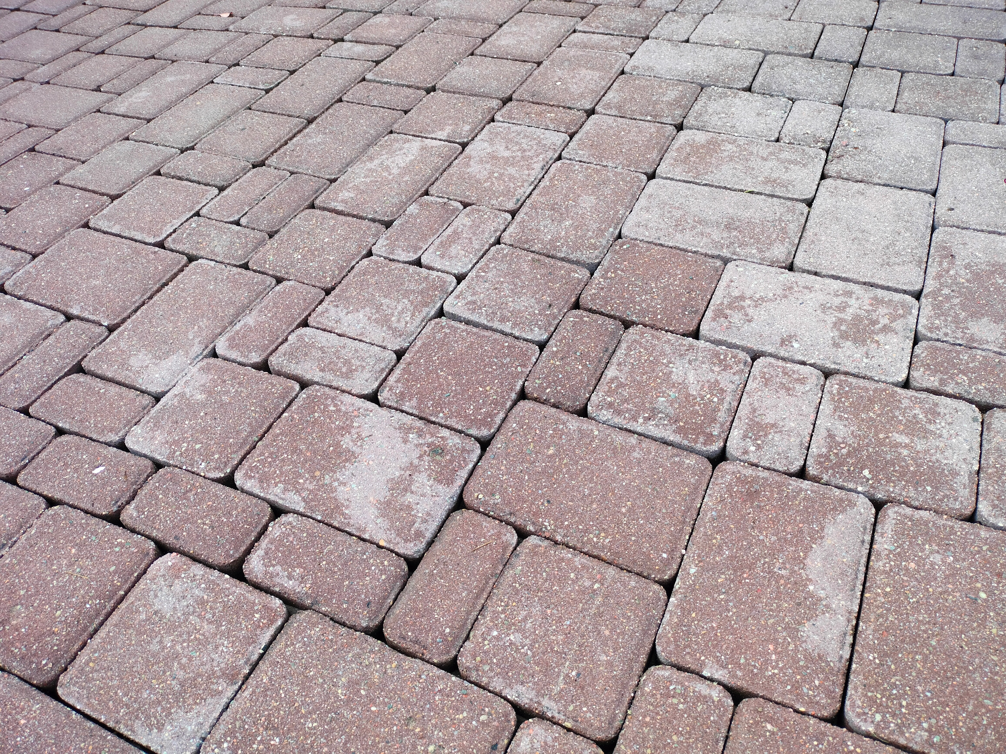 Ułożona, czerwono-szara kostka brukowa w regularnym wzorze. Widoczne drobne nierówności i tekstura materiału, nadająca naturalny wygląd.