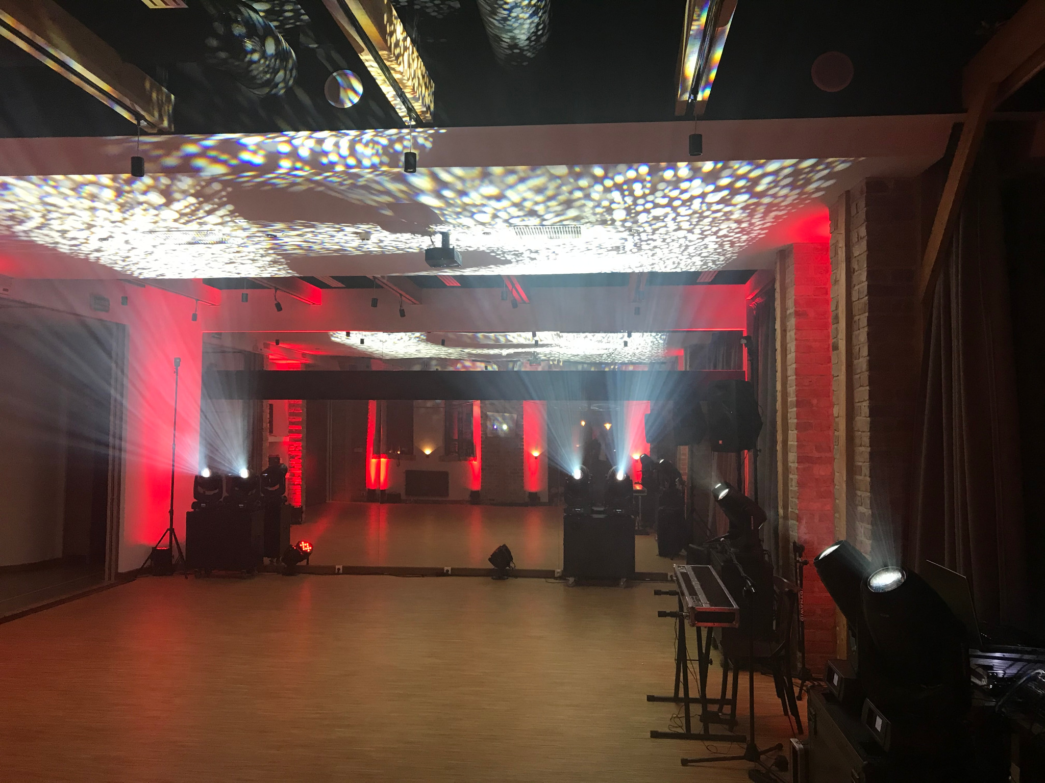 Sala z nagłośnieniem i oświetleniem: reflektory, kolumny głośnikowe, konsoleta. Na suficie widoczne efekty świetlne. Czerwone światło podkreśla ceglane filary.