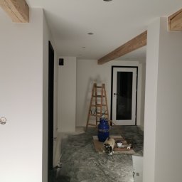 R.S Wykonczenia - Wnętrze w trakcie malowania: białe ściany, drewniane belki, drabina, butla gazowa i nagrzewnica. Widoczne ślady prac malarskich na podłodze.