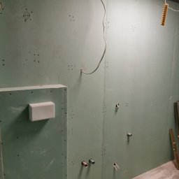 R.S Wykonczenia - Łazienka w trakcie wykańczania: płyty karton-gips, instalacja wodno-kanalizacyjna, przewody elektryczne. Widoczne narzędzia i poziomica.