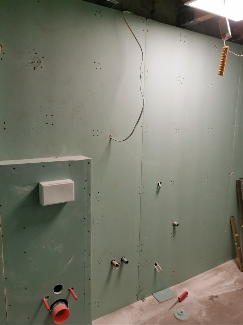 Łazienka w trakcie wykańczania: płyty karton-gips, instalacja wodno-kanalizacyjna, przewody elektryczne. Widoczne narzędzia i poziomica.