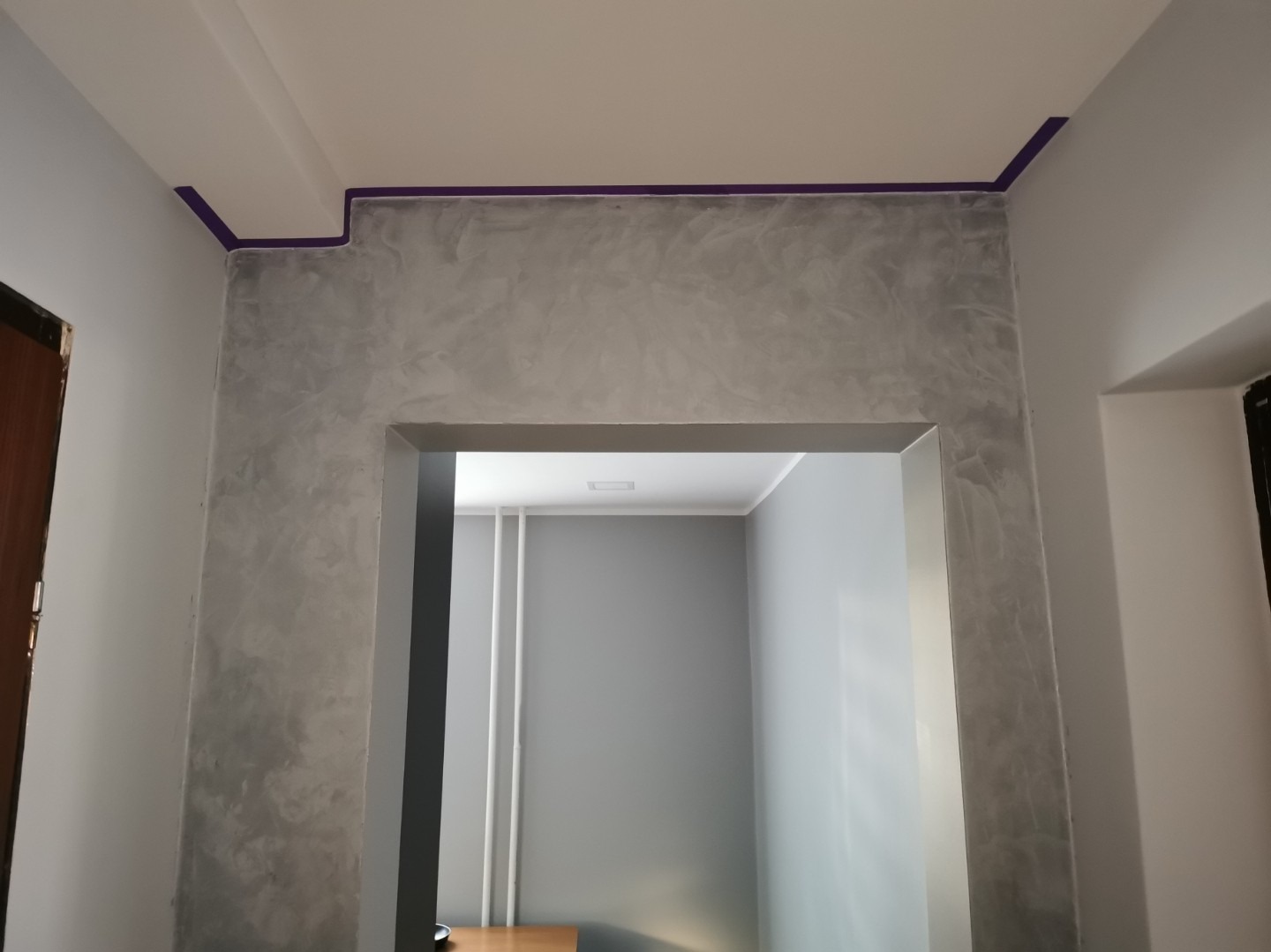 Ściana z efektem dekoracyjnym, zabezpieczona taśmą malarską przy suficie, widok z perspektywy niskiego kąta, wnętrze w szarościach.