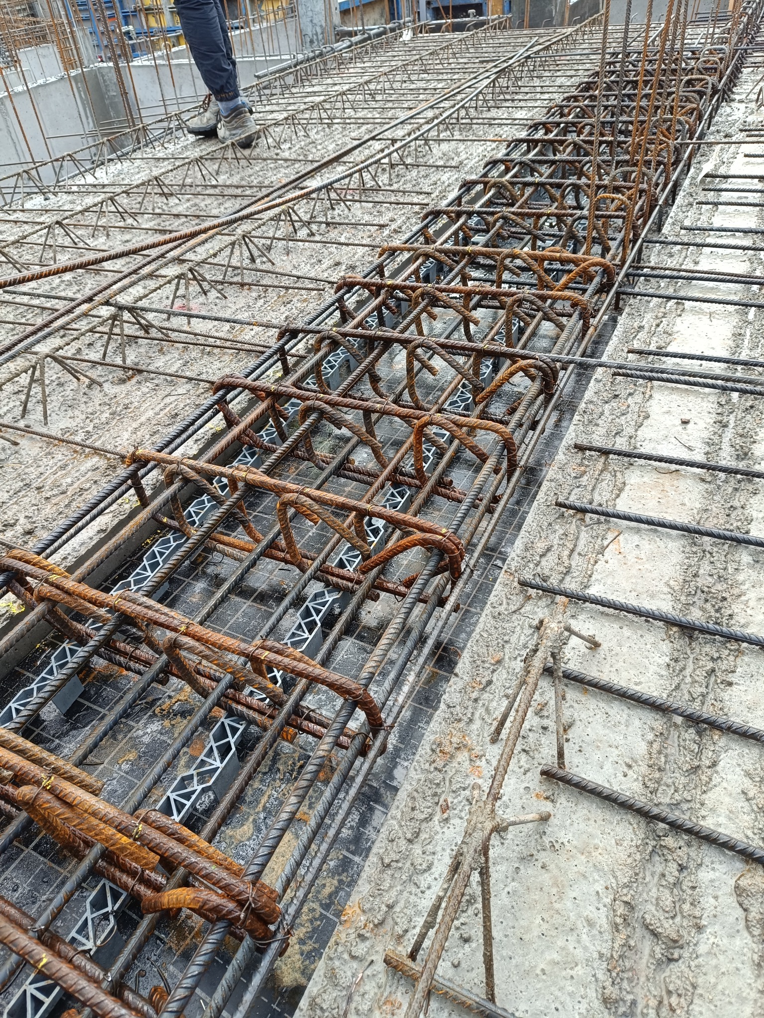 Siatka zbrojeniowa ułożona na betonowym fundamencie z widocznymi plastikowymi dystansami, przygotowana do zalania betonem.