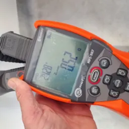 Miernik Sonel MPI-507 podłączony do gniazdka elektrycznego podczas pomiaru napięcia. Na wyświetlaczu widoczny wynik pomiaru. Pomiar rezystancji.