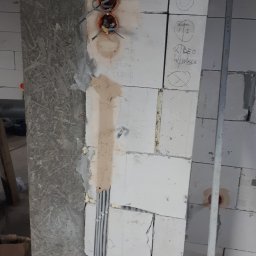 EneGo Michał Pilarski - Instalacja elektryczna w trakcie montażu w Niekłonicach. Widoczne puszki pod gniazdka, przewody i fragment ściany z bloczków z naniesionymi oznaczeniami.