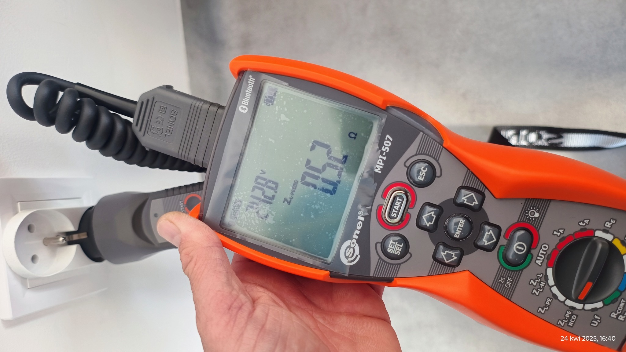 Miernik Sonel MPI-507 podłączony do gniazdka elektrycznego podczas pomiaru napięcia. Na wyświetlaczu widoczny wynik pomiaru. Pomiar rezystancji.