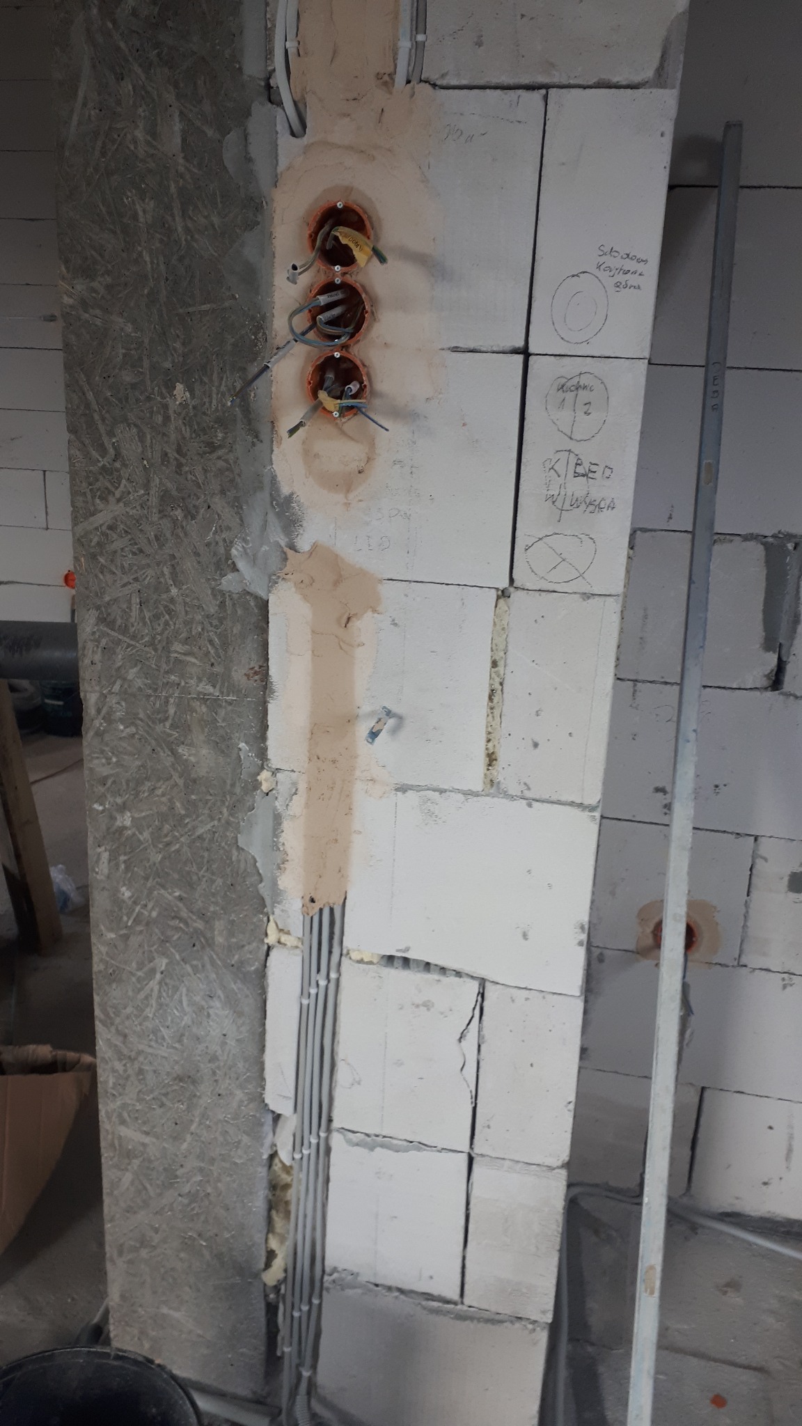Instalacja elektryczna w trakcie montażu w Niekłonicach. Widoczne puszki pod gniazdka, przewody i fragment ściany z bloczków z naniesionymi oznaczeniami.