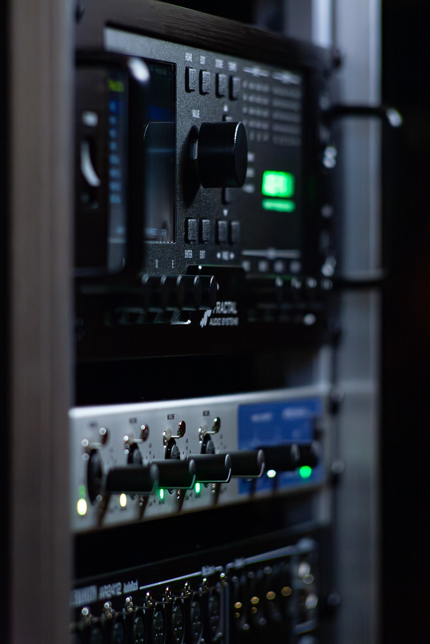 Zamknięty kadr racka ze sprzętem audio: procesor Fractal Audio Systems, preamper mikrofonowy z podświetlonymi diodami, panel krosowniczy z gniazdami XLR.