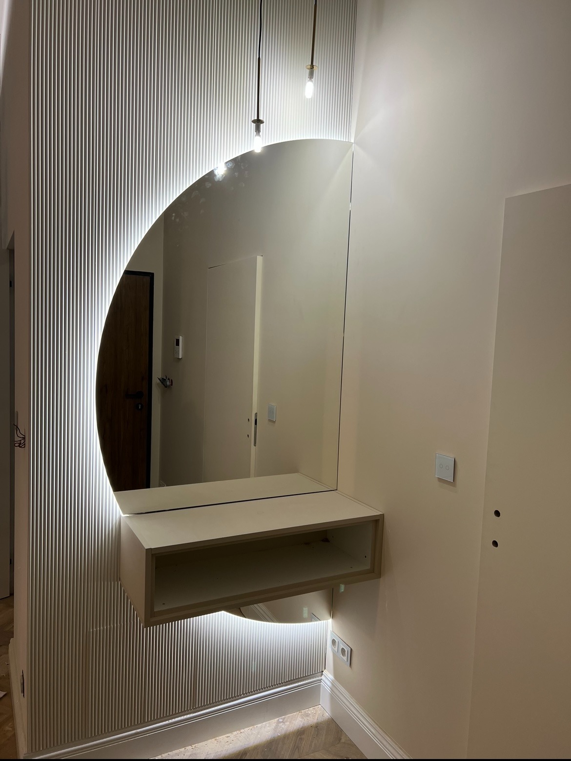 Nowoczesne lustro z podświetleniem LED w kształcie półksiężyca, zamontowane na ścianie z dekoracyjnymi panelami. Minimalistyczny design, ciepłe oświetlenie.