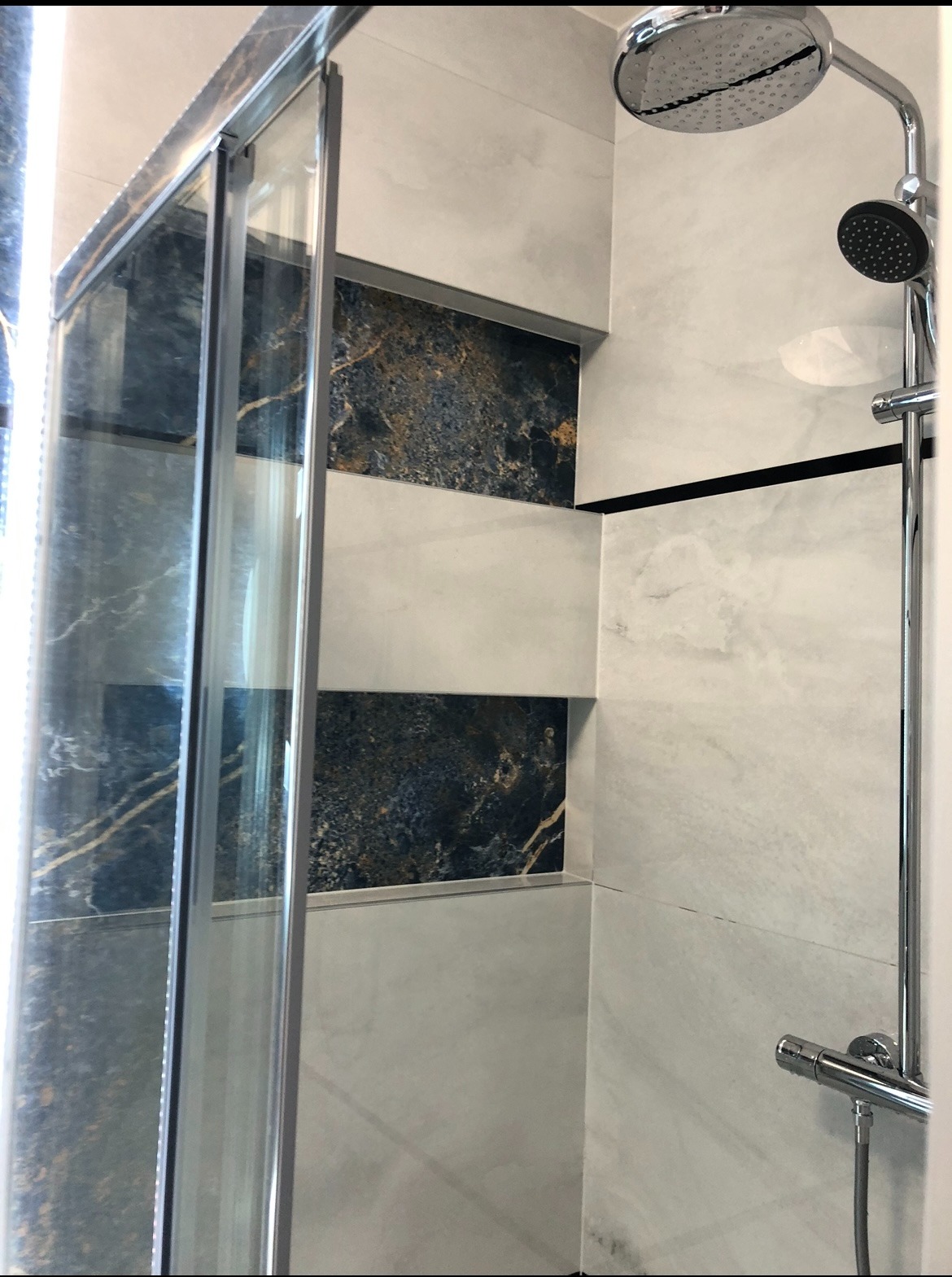 Nowoczesna kabina prysznicowa z marmurowymi płytkami w odcieniach bieli i granatu, chromowana armatura, deszczownica. Wykończenie łazienki w eleganckim stylu.