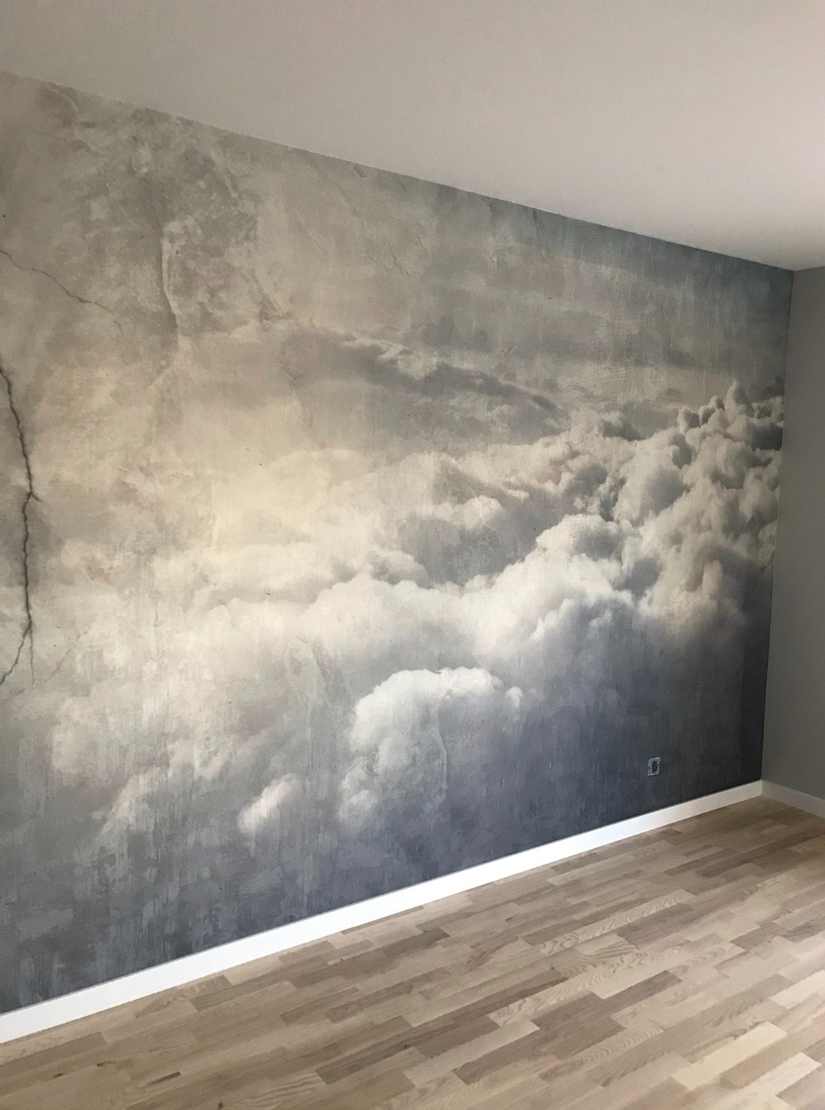Ściana z efektem chmur w pokoju w Warszawie. Dekoracyjna faktura przypomina niebo. Jasna podłoga z paneli i biała listwa przypodłogowa.