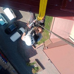 SkyRope Usługi Wysokościowe Paweł Krzystek - Pracownik w kasku, zabezpieczony liną, uszczelnia element dachu w Bytomiu, widok z góry na budynek z czerwonym dachem i zaparkowane samochody.