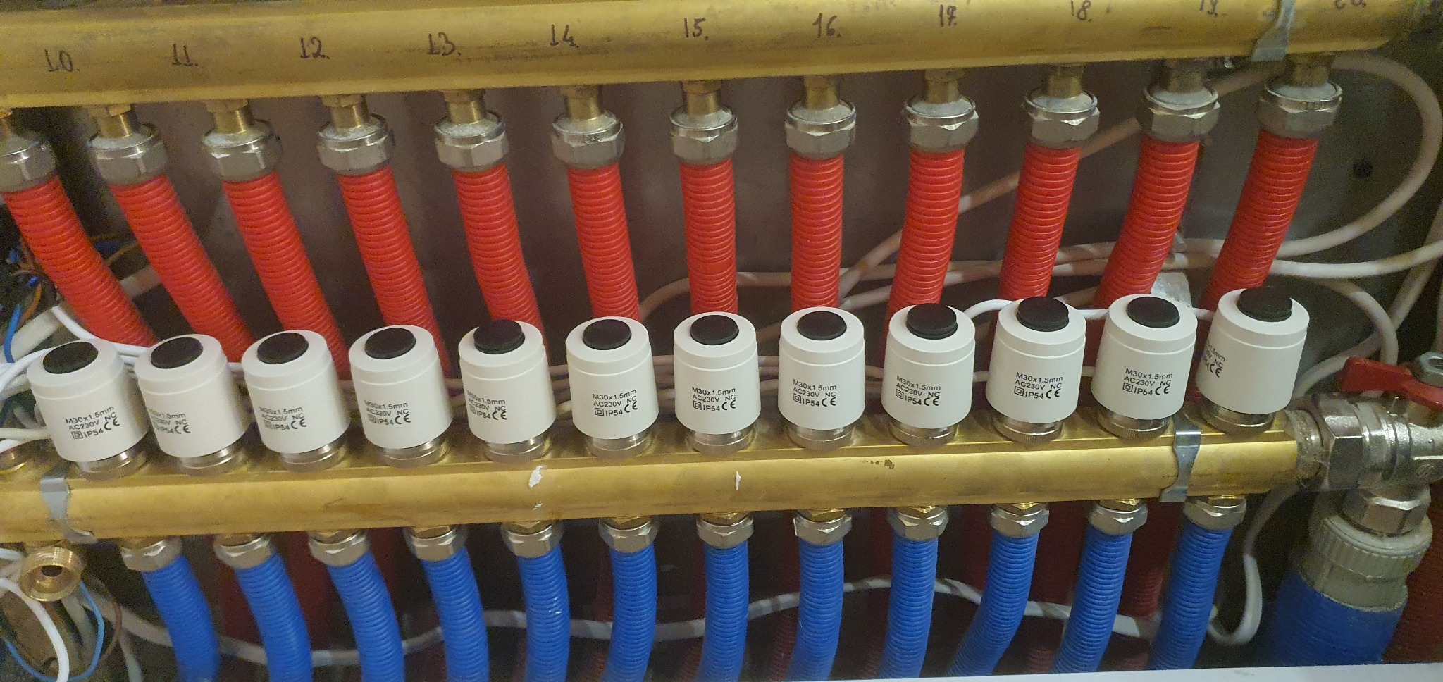Rozdzielacz ogrzewania podłogowego z termostatami M30x1.5mm, rurami w osłonie karbowanej czerwonej i niebieskiej, oznaczony numerami od 10 do 19.