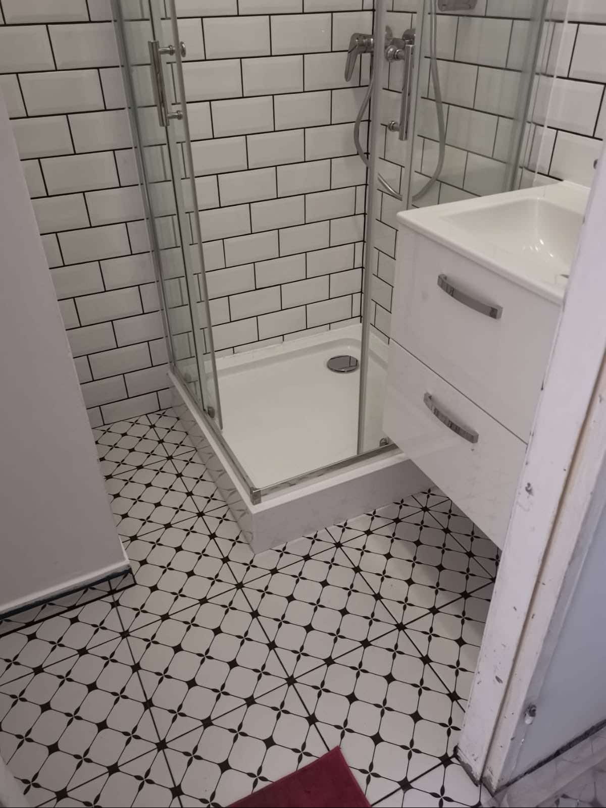 Wyremontowana łazienka z kabiną prysznicową, białą umywalką z szafką i czarno-białą podłogą w geometryczny wzór; białe płytki ścienne w stylu cegiełek.