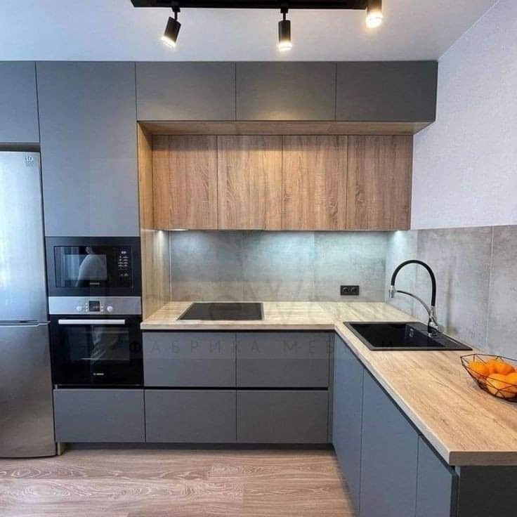 Szara kuchnia z drewnianymi akcentami i czarnym zlewem narożnym, oświetlona punktowymi lampami sufitowymi, z widocznym fragmentem podłogi z paneli.