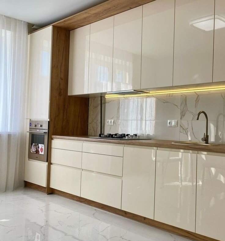 Nowoczesna kuchnia na wymiar z białymi, lakierowanymi frontami, drewnianym blatem i marmurową ścianą nad blatem, widziana z niskiego kąta.