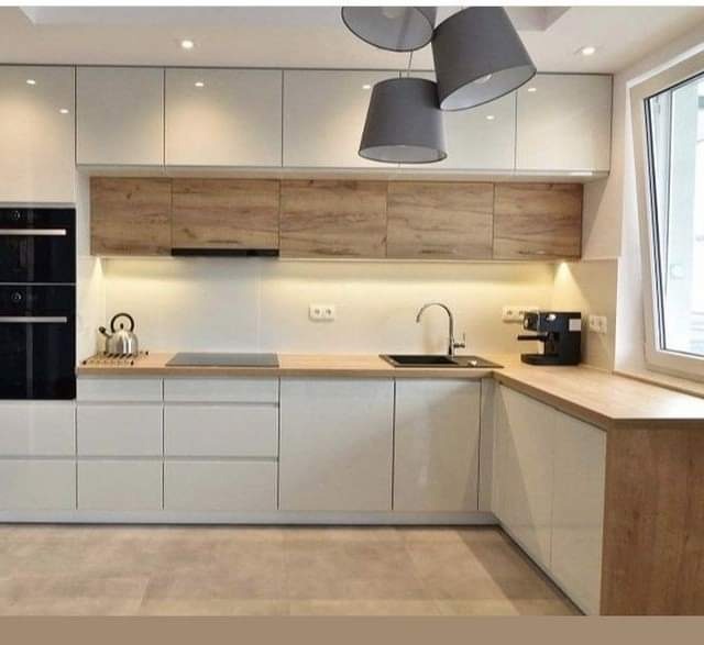 Nowoczesna kuchnia z białymi frontami szafek i drewnianym blatem, oświetlenie LED podszafkowe, czarny piekarnik w zabudowie, minimalistyczny zlew i ekspres do kawy na blacie.