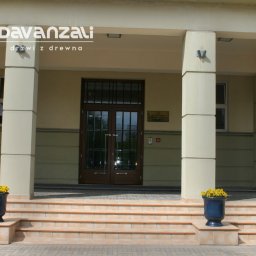 Davanzali -drzwi z drewna - Eleganckie, dwuskrzydłowe drzwi wejściowe z ciemnego drewna, z podziałami szprosowymi, umieszczone w portyku z kolumnami. Donice z żółtymi kwiatami po bokach schodów.