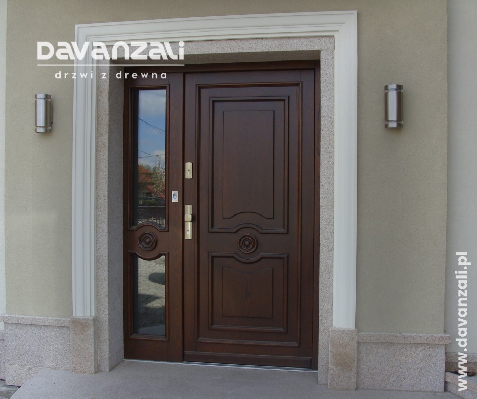 Eleganckie, brązowe drzwi wejściowe z bocznym przeszkleniem, otoczone kamienną ramą i oświetlone dwoma cylindrycznymi lampami ściennymi.