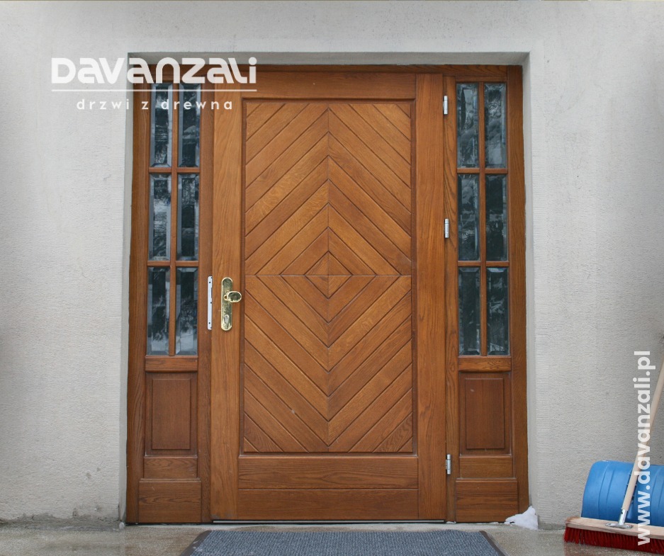 Frontowe ujęcie solidnych, drewnianych drzwi zewnętrznych z bocznymi szybkami, zdobionych wzorem rombów. Widoczny fragment wycieraczki i szczotki.