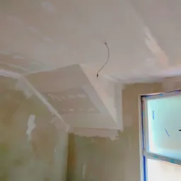 Sufit poddasza po montażu konstrukcji z profili i płyt, widoczne ślady szpachlowania i wystający kabel oświetleniowy, okno w tle.