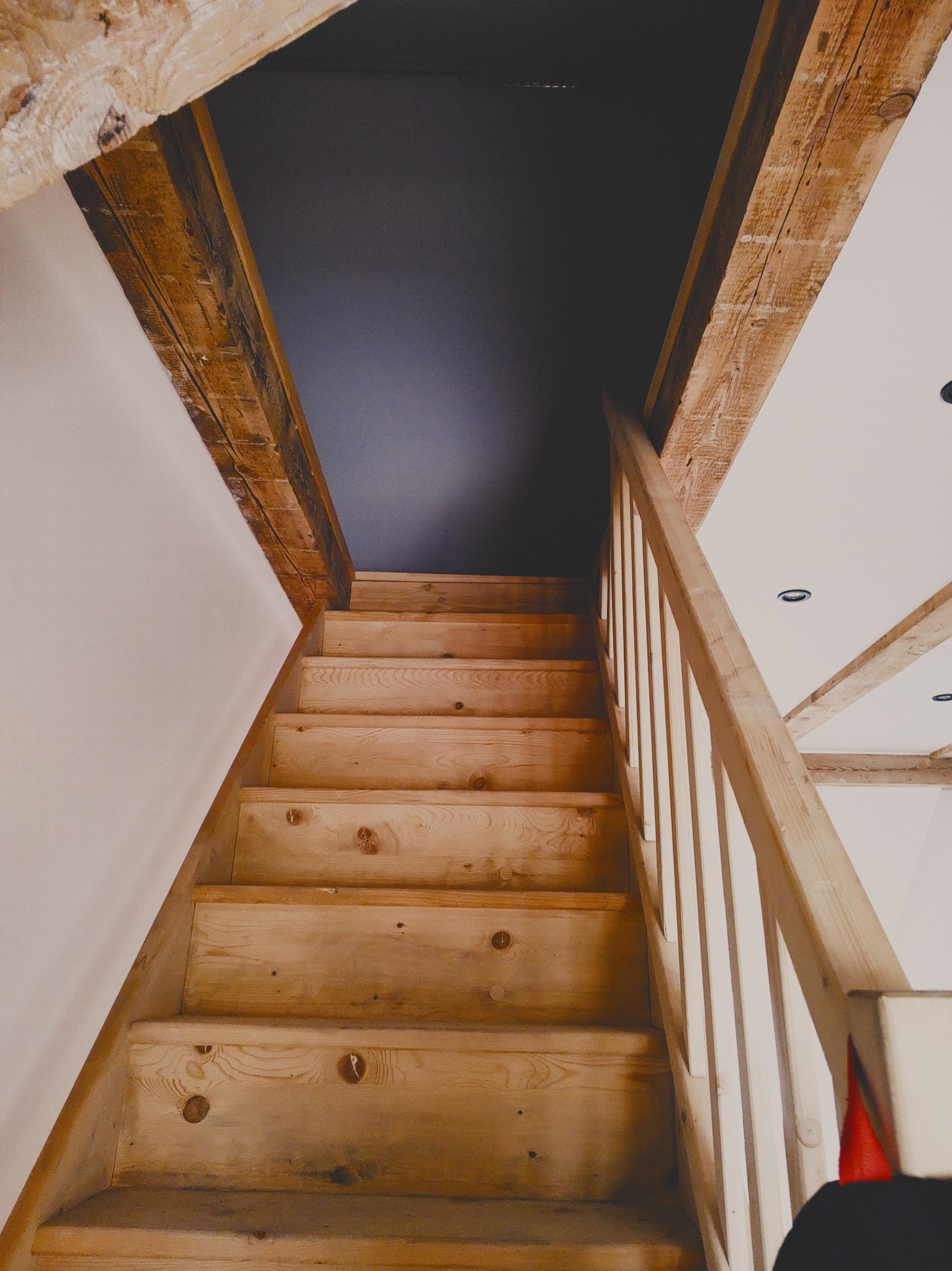 Drewniane schody z balustradą w domu we Wrocławiu, widok z dołu, surowe drewno, widoczne belki stropowe, ściany przygotowane do wykończenia.