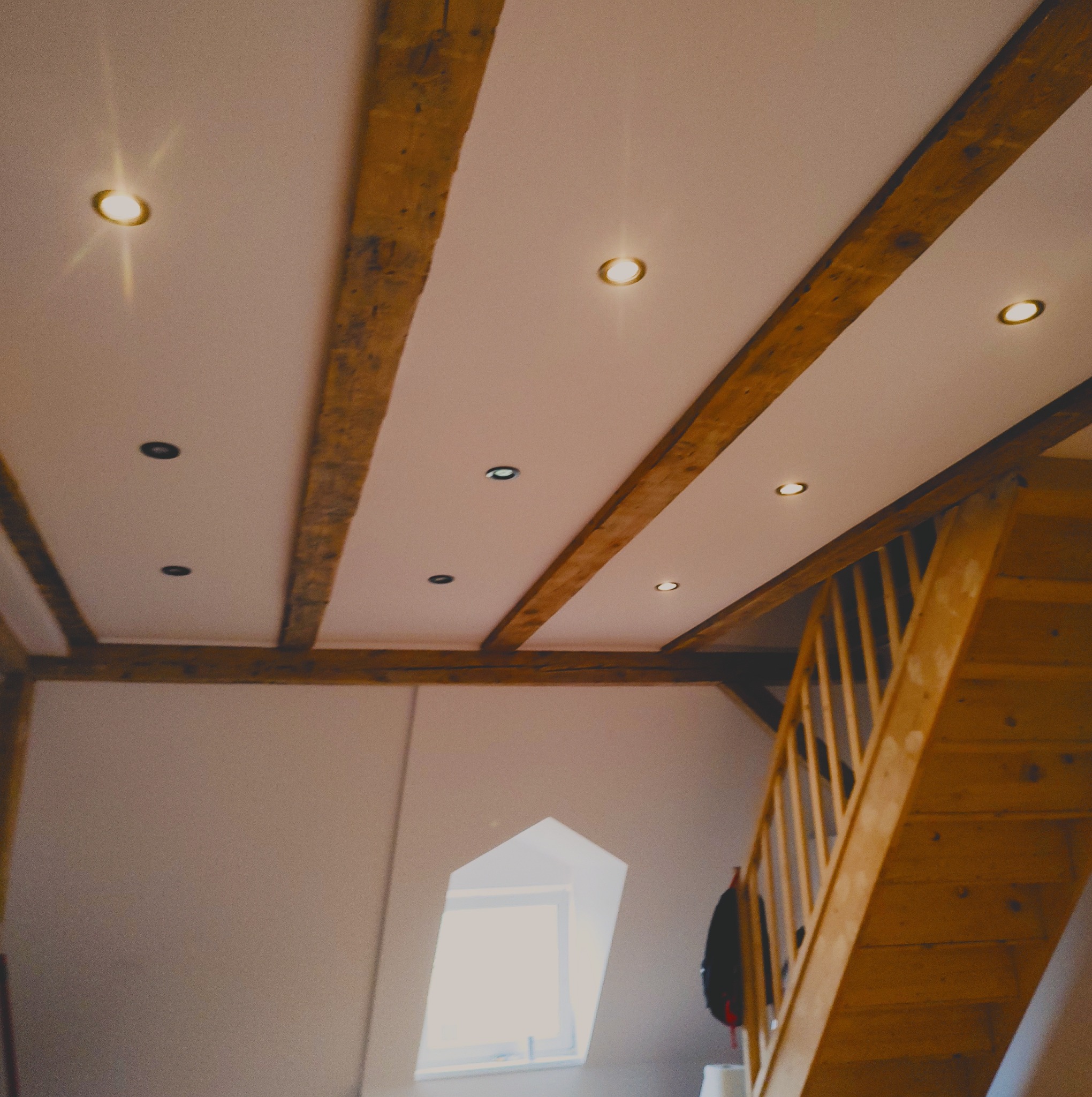 Poddasze po remoncie z drewnianymi belkami stropowymi, oświetleniem punktowym i drewnianymi schodami