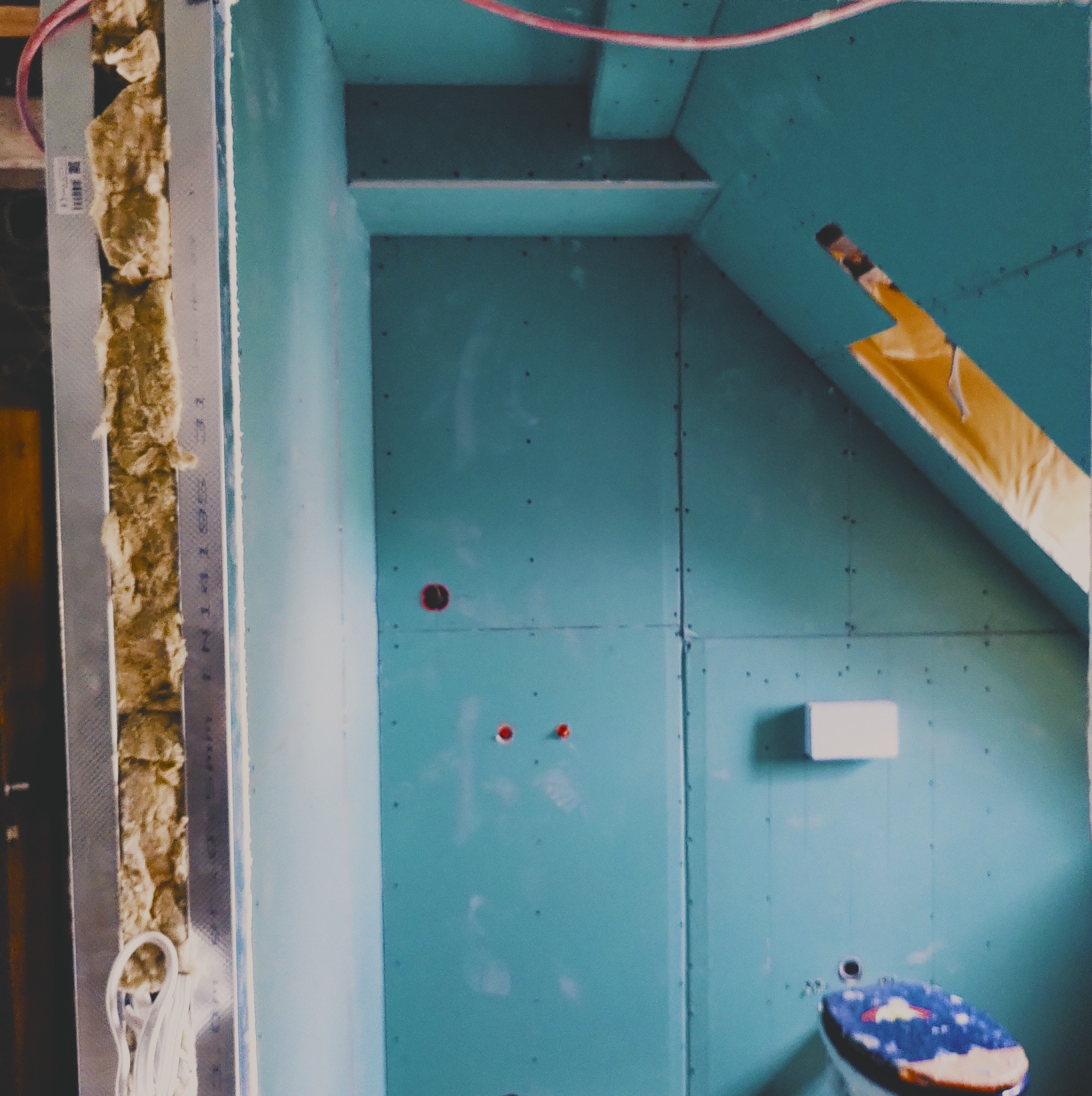 Poddasze w trakcie adaptacji: widoczna izolacja wełną mineralną w metalowym stelażu, niebieskie płyty kartonowo-gipsowe, instalacja elektryczna i otwory pod gniazdka.