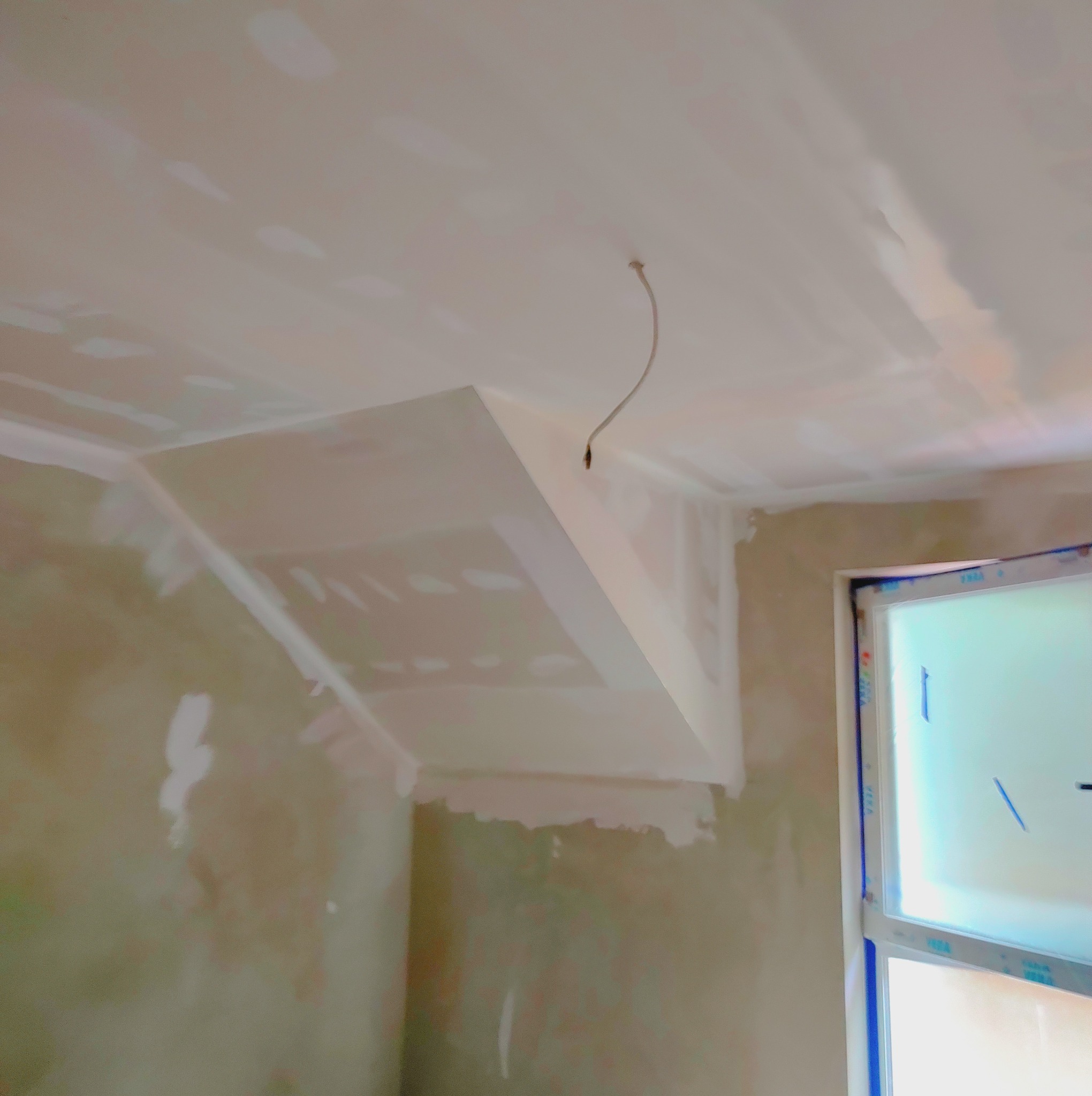 Sufit poddasza po montażu konstrukcji z profili i płyt, widoczne ślady szpachlowania i wystający kabel oświetleniowy, okno w tle.