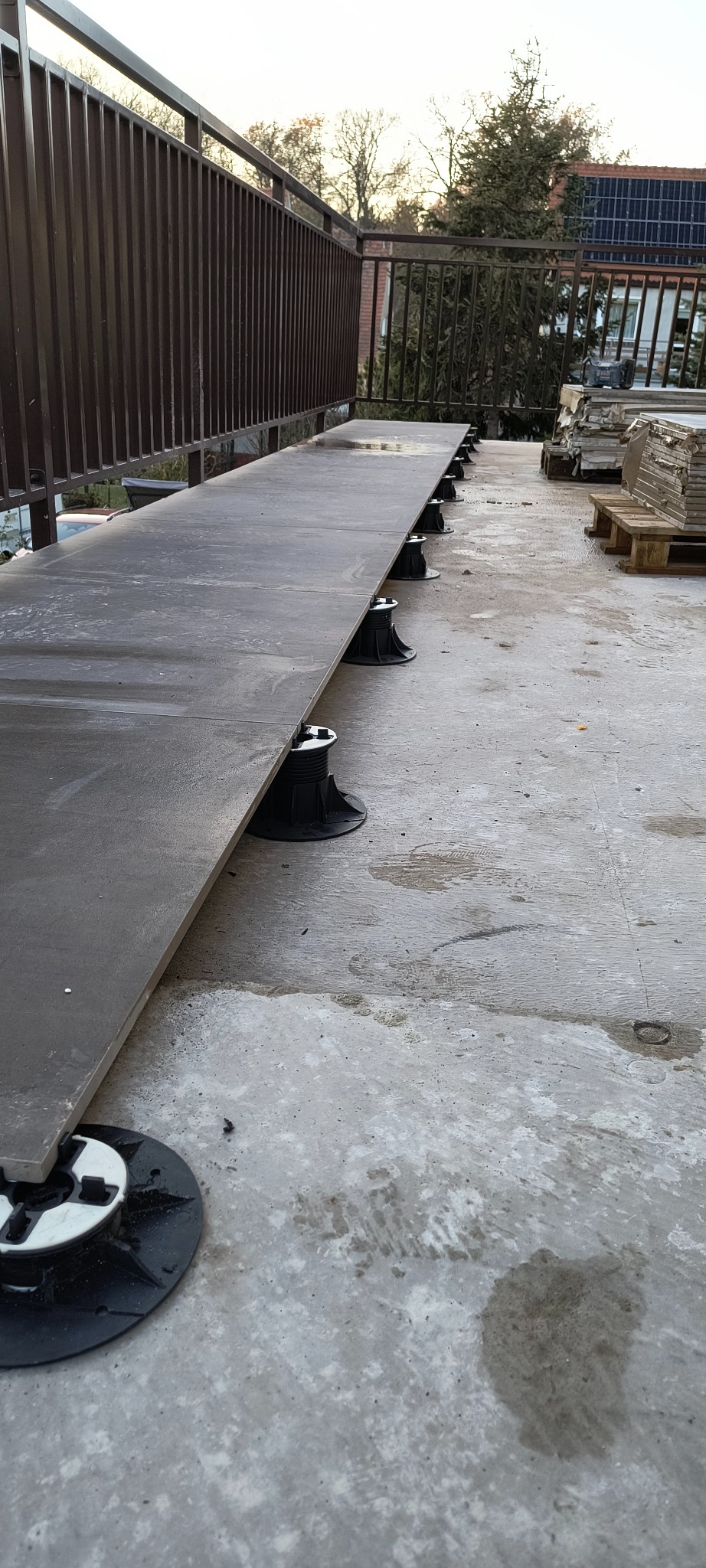 Montaż płytek tarasowych na regulowanych wspornikach na balkonie. Widoczne płytki, wsporniki, balustrada i elementy otoczenia.