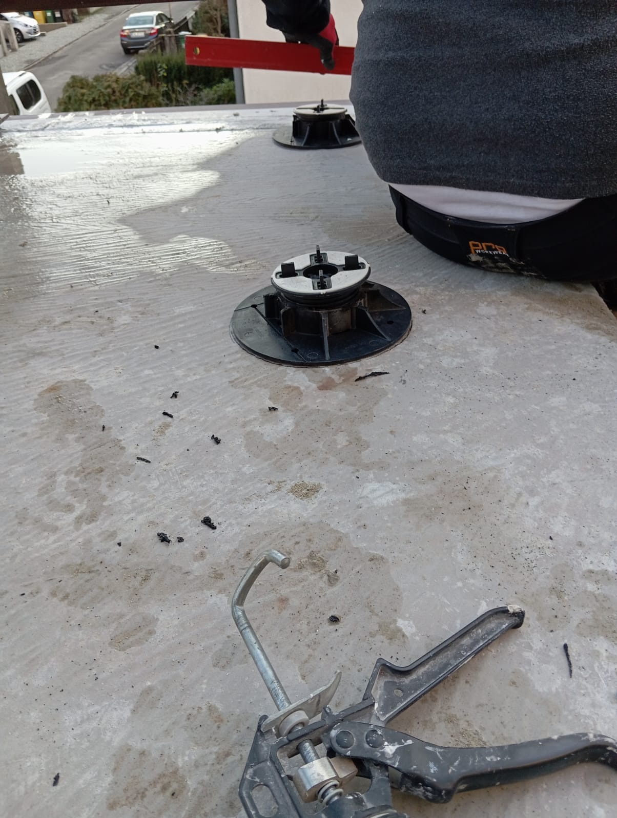 Montaż regulowanych wsporników tarasowych na betonowej powierzchni. Widoczny pistolet do kleju i poziomica, co sugeruje precyzyjne ustawianie wysokości.