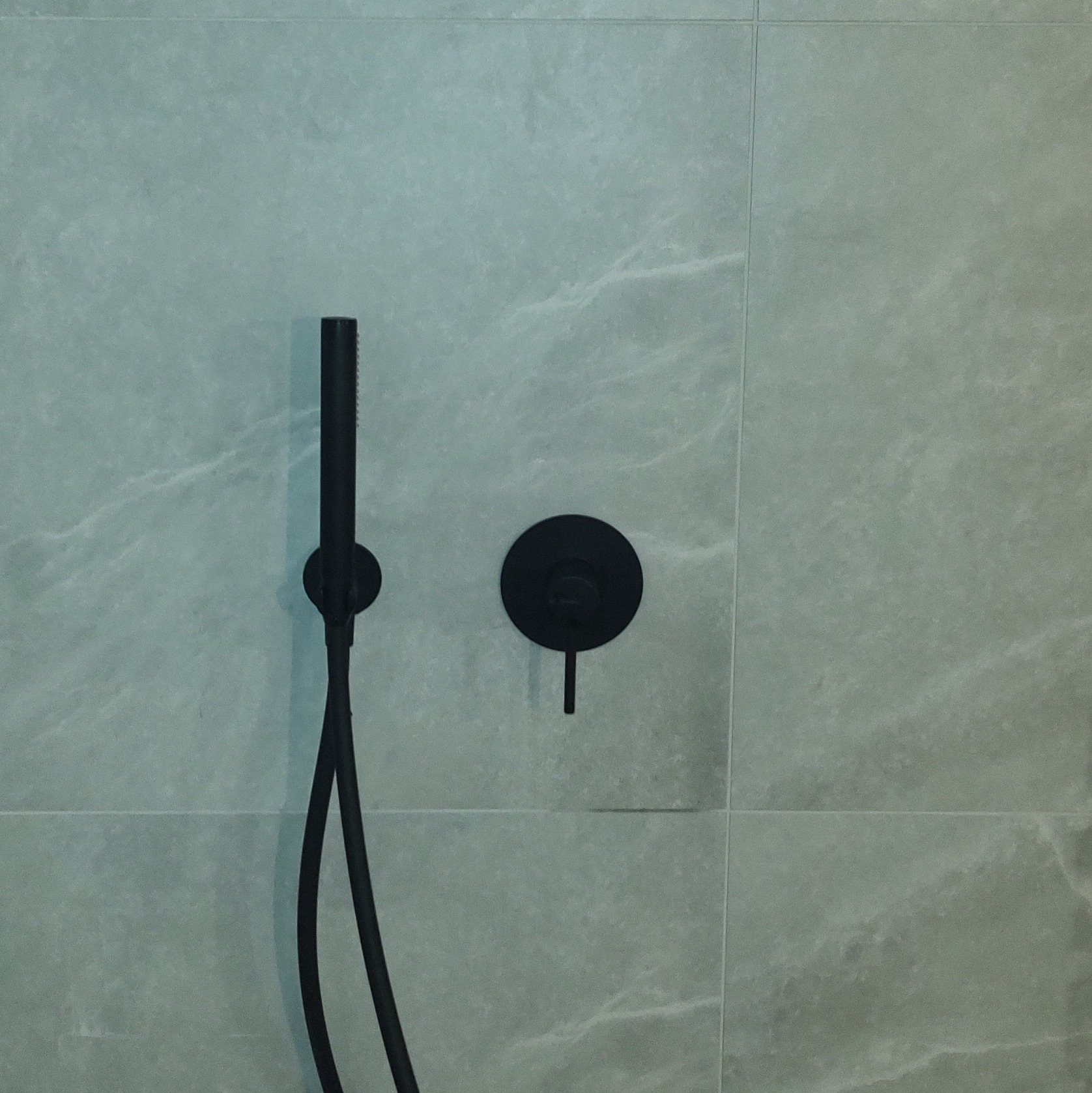 Minimalistyczna łazienka: czarna bateria natryskowa i panel sterujący na tle szarych, marmurkowych płytek. Nowoczesny design, precyzyjne wykończenie.