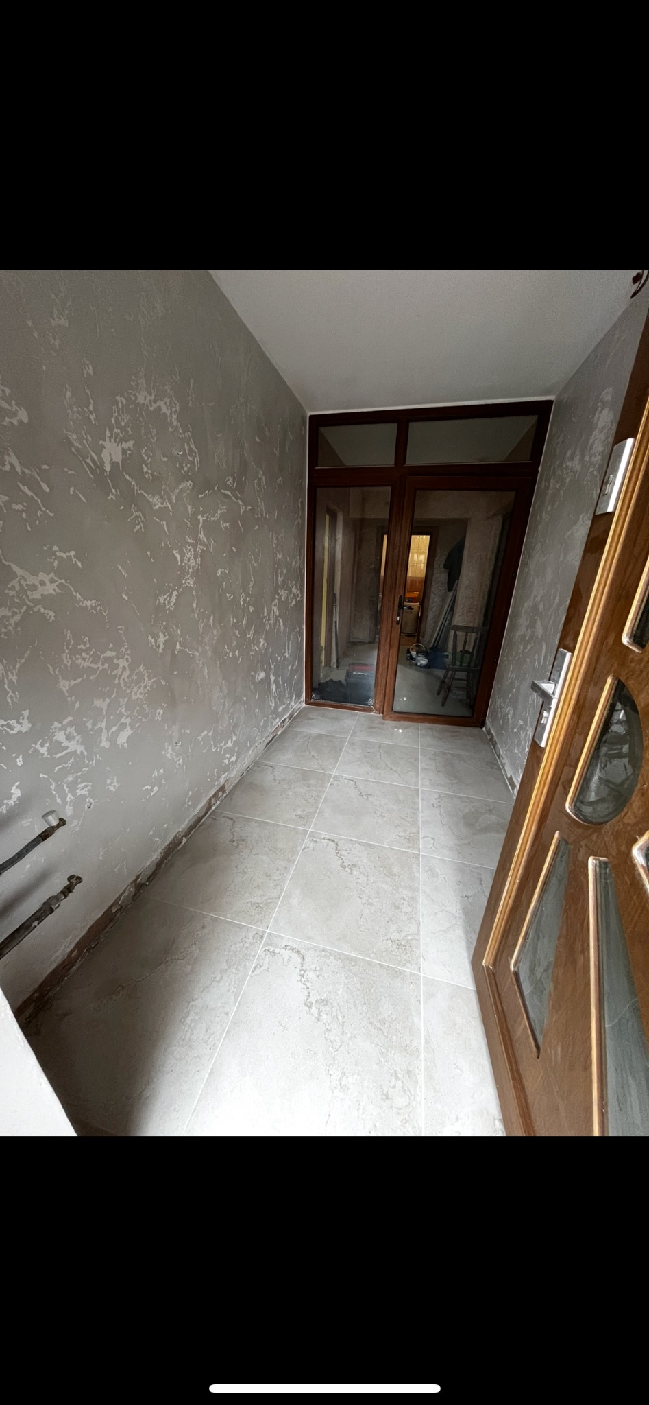 Korytarz po remoncie: szare ściany z efektem dekoracyjnym, jasne płytki podłogowe, drewniane drzwi z szybami. Widoczne niedokończone prace przy podłodze.