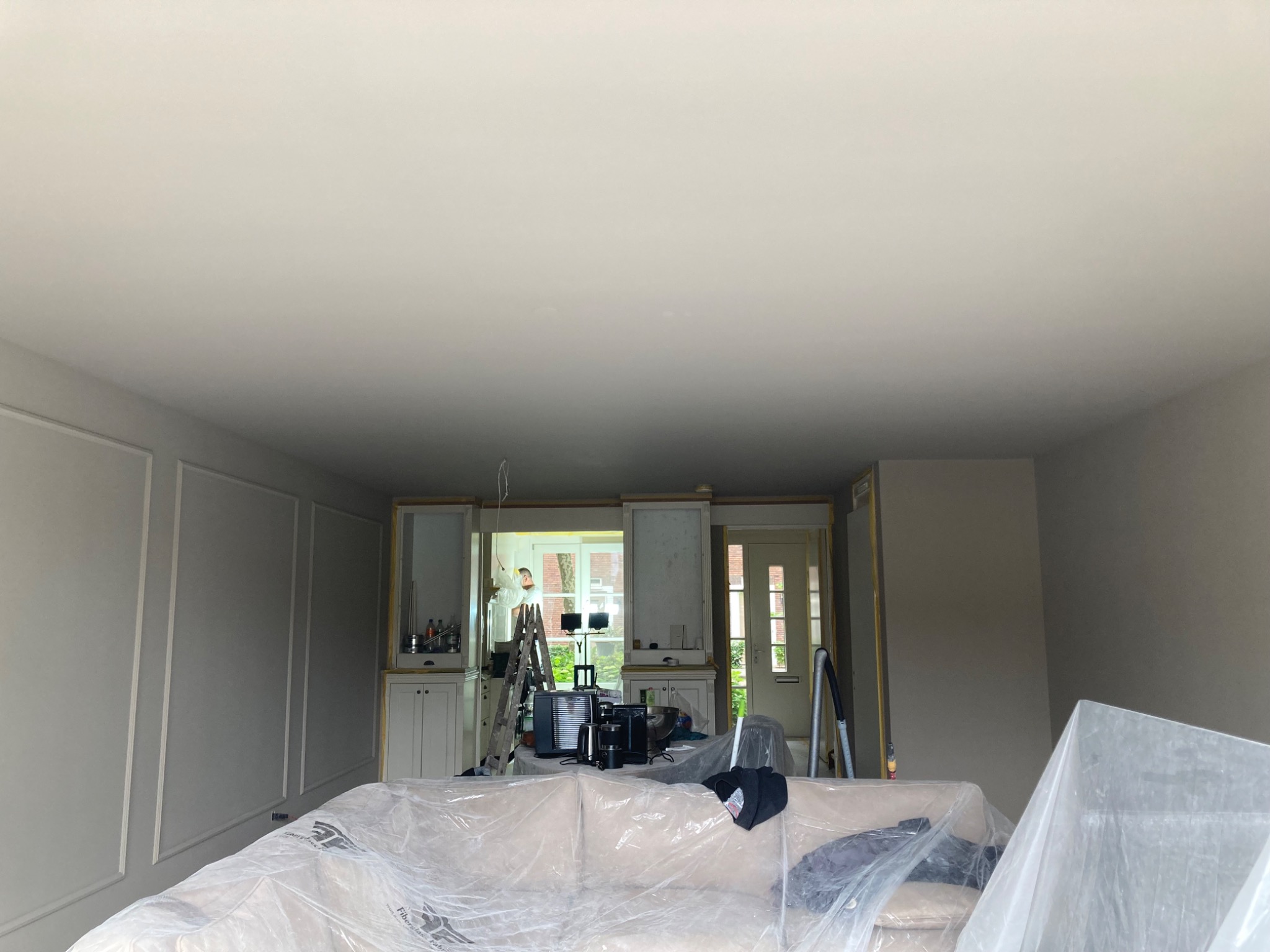 Jasne wnętrze w trakcie odświeżania: ściany po malowaniu, meble zabezpieczone folią, drabina malarska. Widoczne detale architektoniczne.