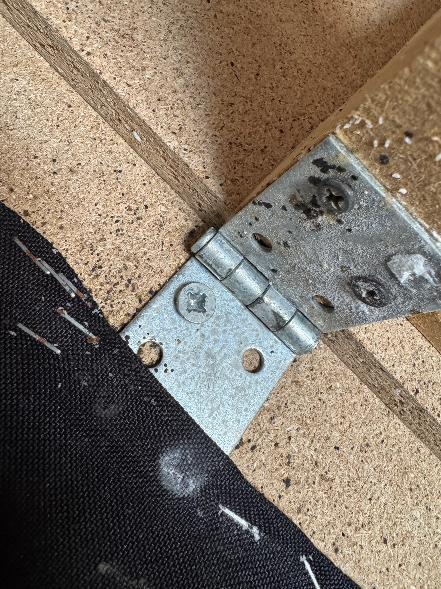 Fragment mebla tapicerowanego z widocznym zawiasem, zszywkami tapicerskimi i śladami białego proszku, być może po środkach owadobójczych.