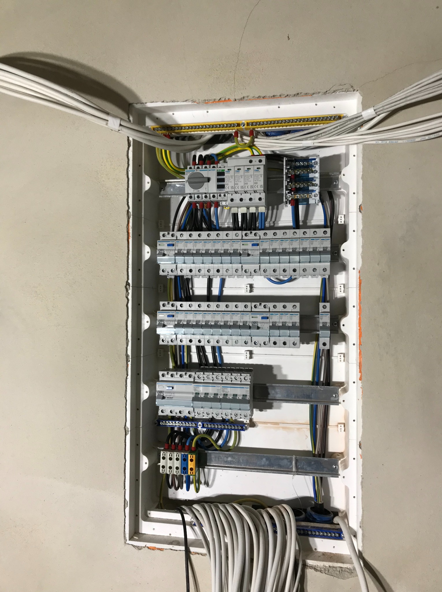 Rozdzielnica elektryczna wnękowa z zabezpieczeniami, widoczne kable wchodzące i wychodzące, ściana w stanie surowym.