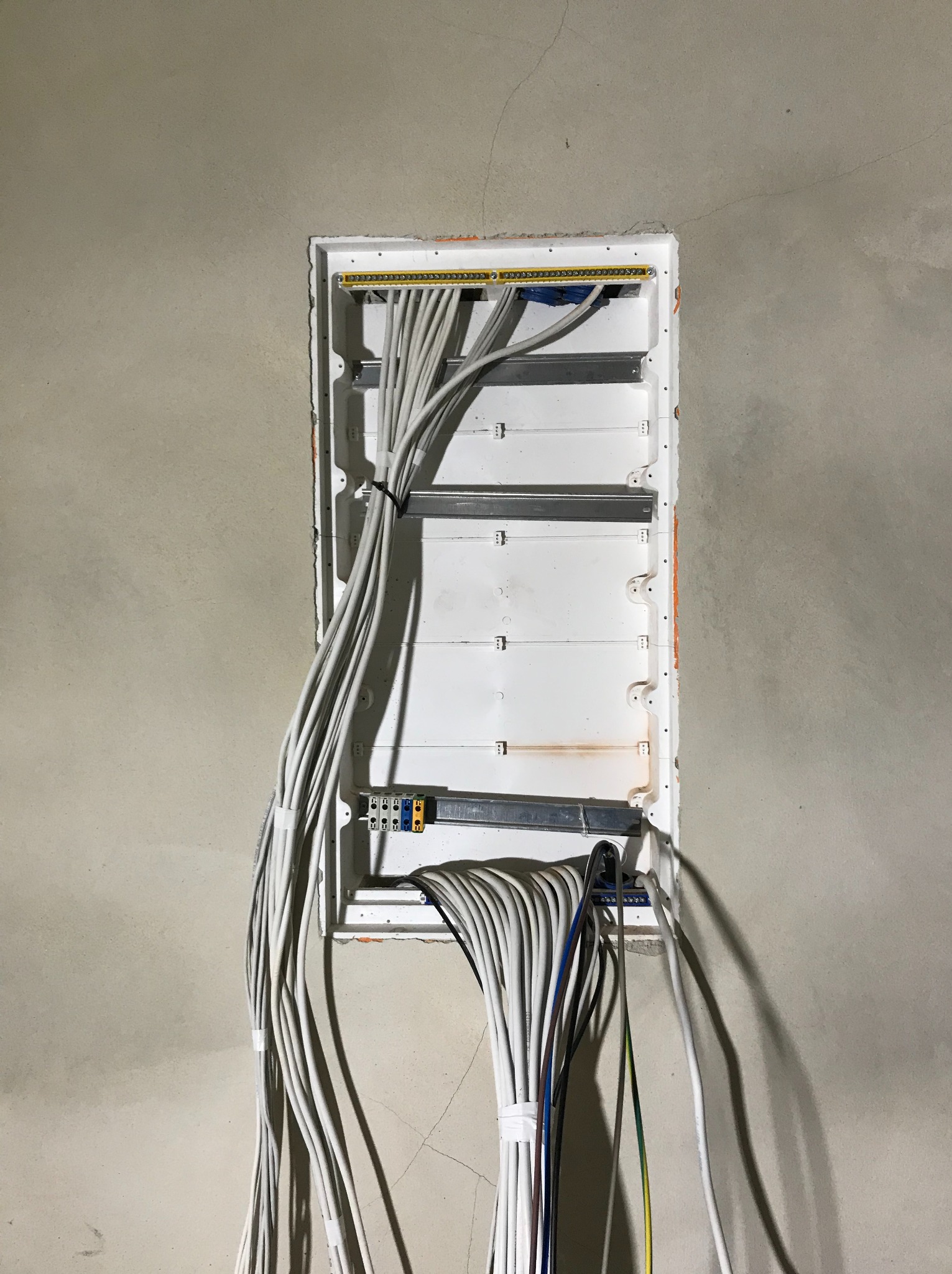 Rozdzielnica elektryczna w trakcie montażu, widoczne liczne przewody wchodzące do skrzynki, szare ściany w tle.