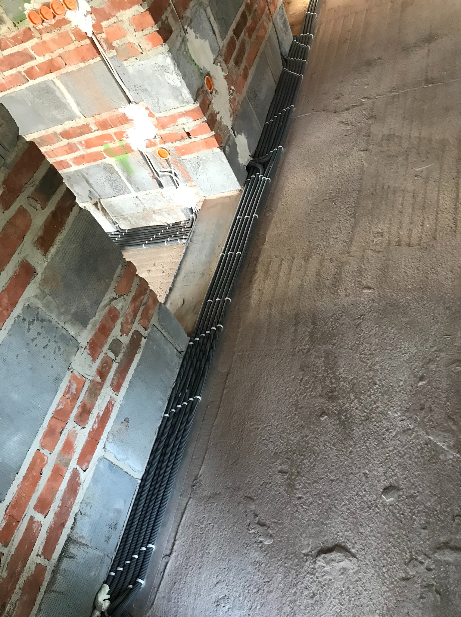 Wiązka przewodów elektrycznych w peszlach, równolegle ułożonych wzdłuż surowej ściany w budynku w Woli Żarczyckiej, widoczne puszki instalacyjne w murze z cegły.