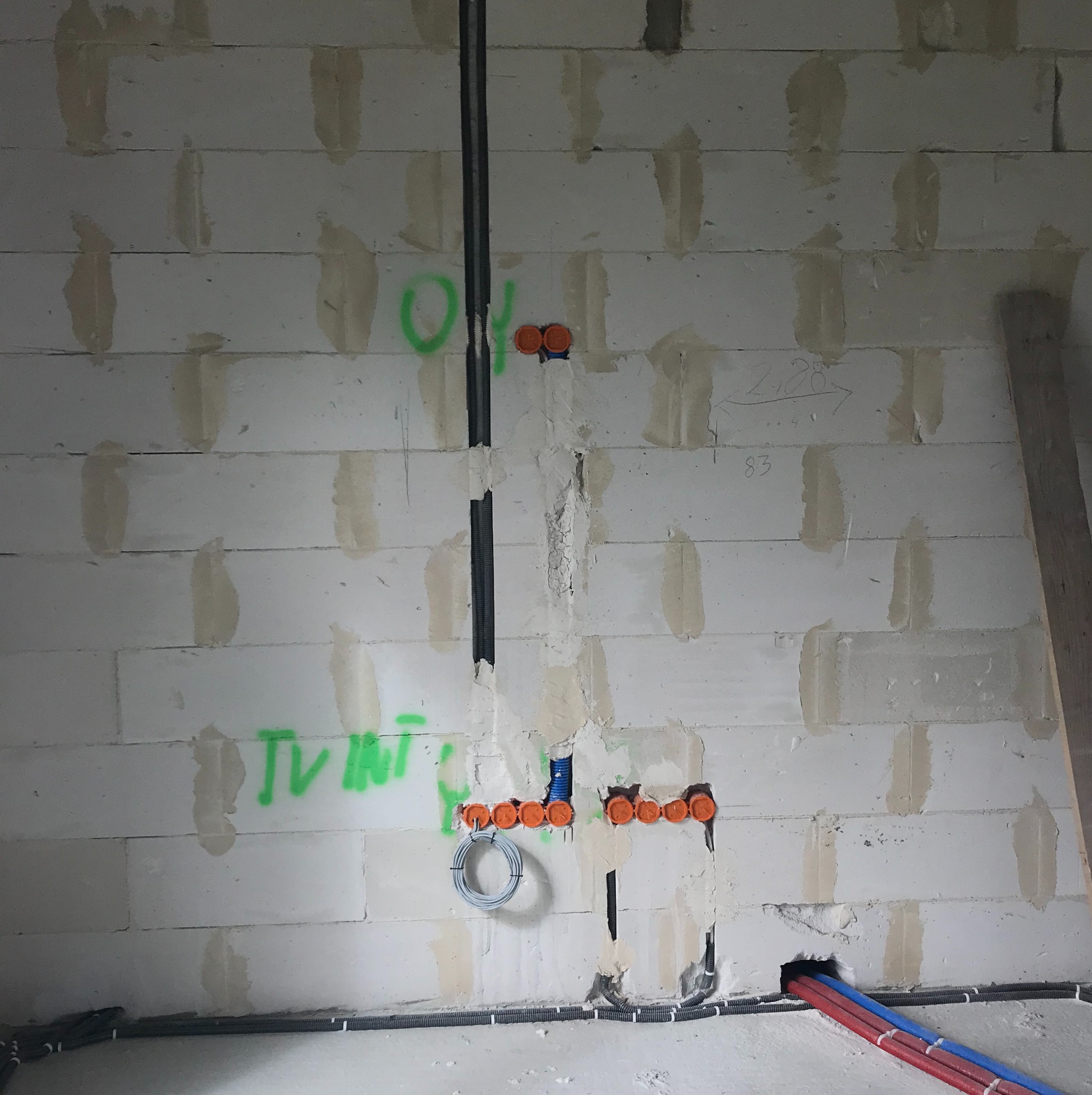 Ściana z betonu komórkowego w trakcie prac instalacyjnych: widoczne kable w peszlach, puszki instalacyjne pomarańczowe, przewody elektryczne zwinięte w pętlę, oraz rury instalacyjne czerwone...