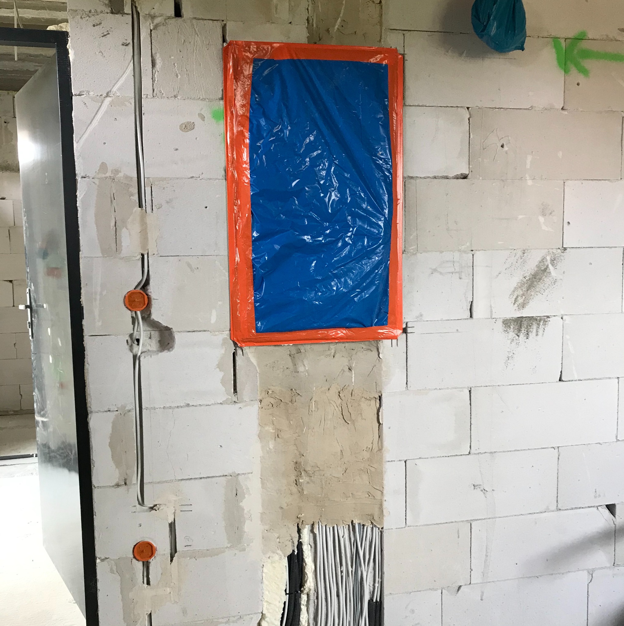 Ściana z betonu komórkowego w trakcie prac elektrycznych: widoczne kable w bruzdach, zakryty otwór folią ochronną, puszki instalacyjne zamontowane.
