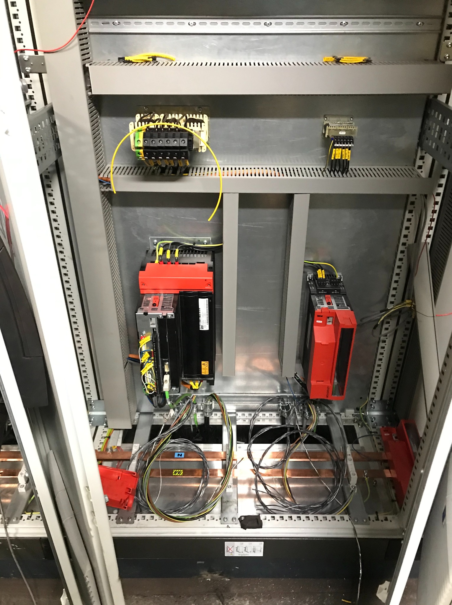 Wnętrze szafy elektrycznej z zamontowanymi modułami sterującymi, widoczne kable i przewody podłączone do urządzeń, szyny miedziane na spodzie szafy.